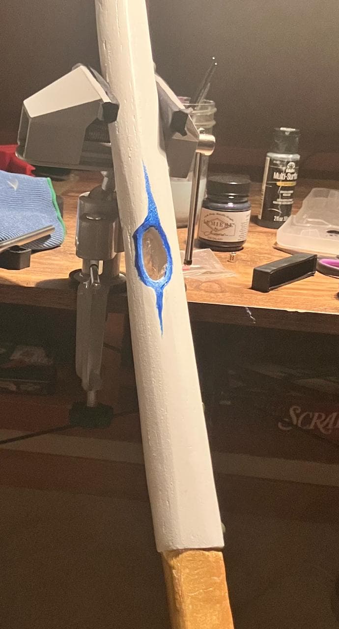 White wooden sword with blue hand painted detail held in a workshop vise