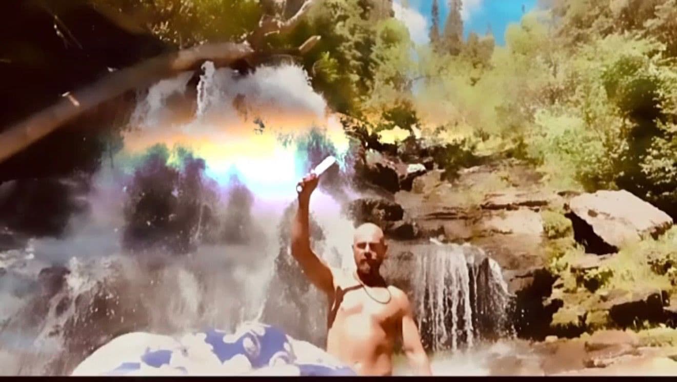 Ethan standing beneath a waterfall with a rainbow in the mist